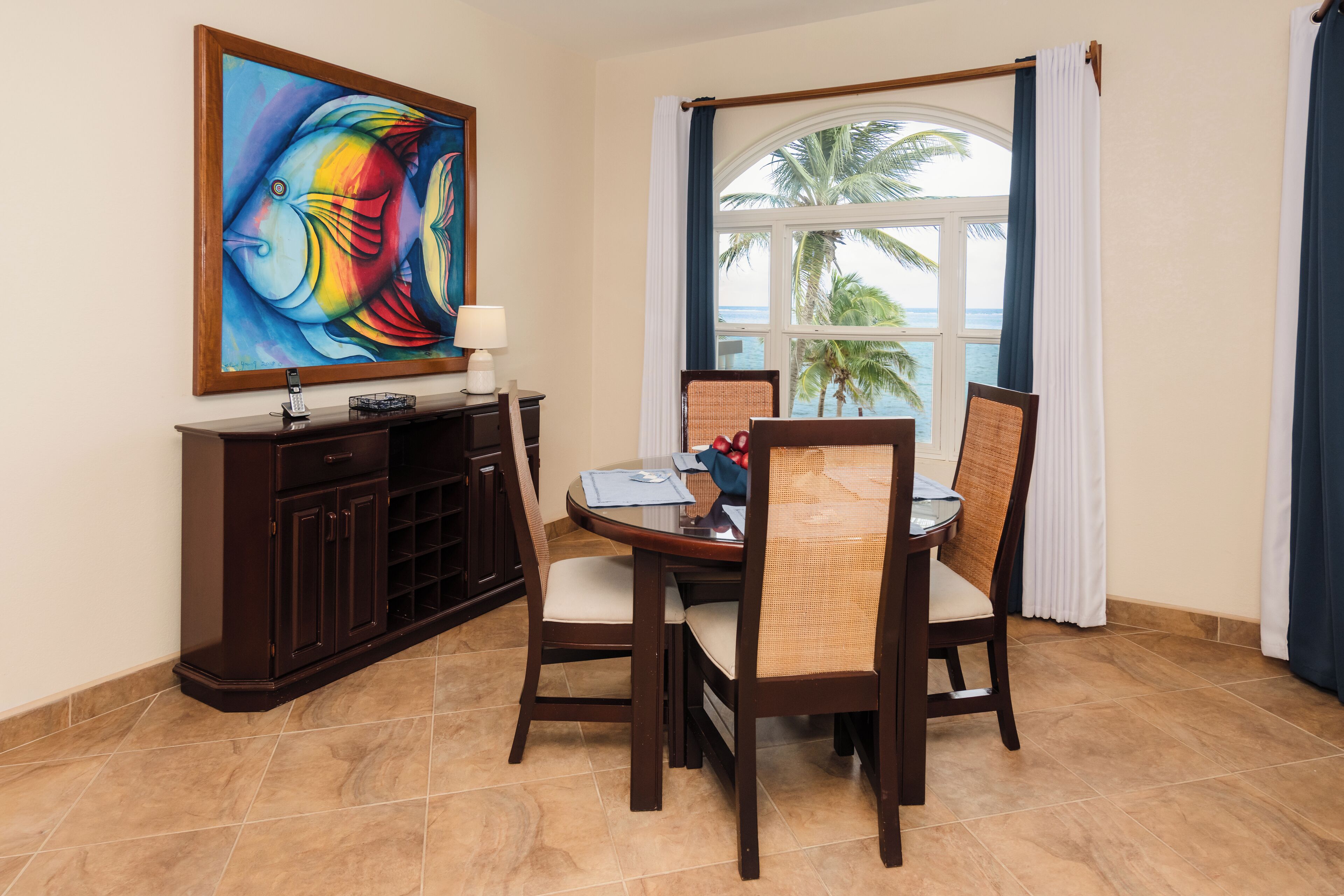 A dining area with a round table, four chairs, a dark wooden cabinet, and a painting on the wall.