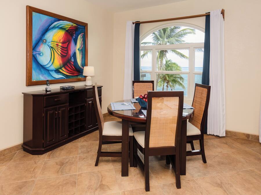 A dining area with a round table, four chairs, a dark wooden cabinet, and a painting on the wall.