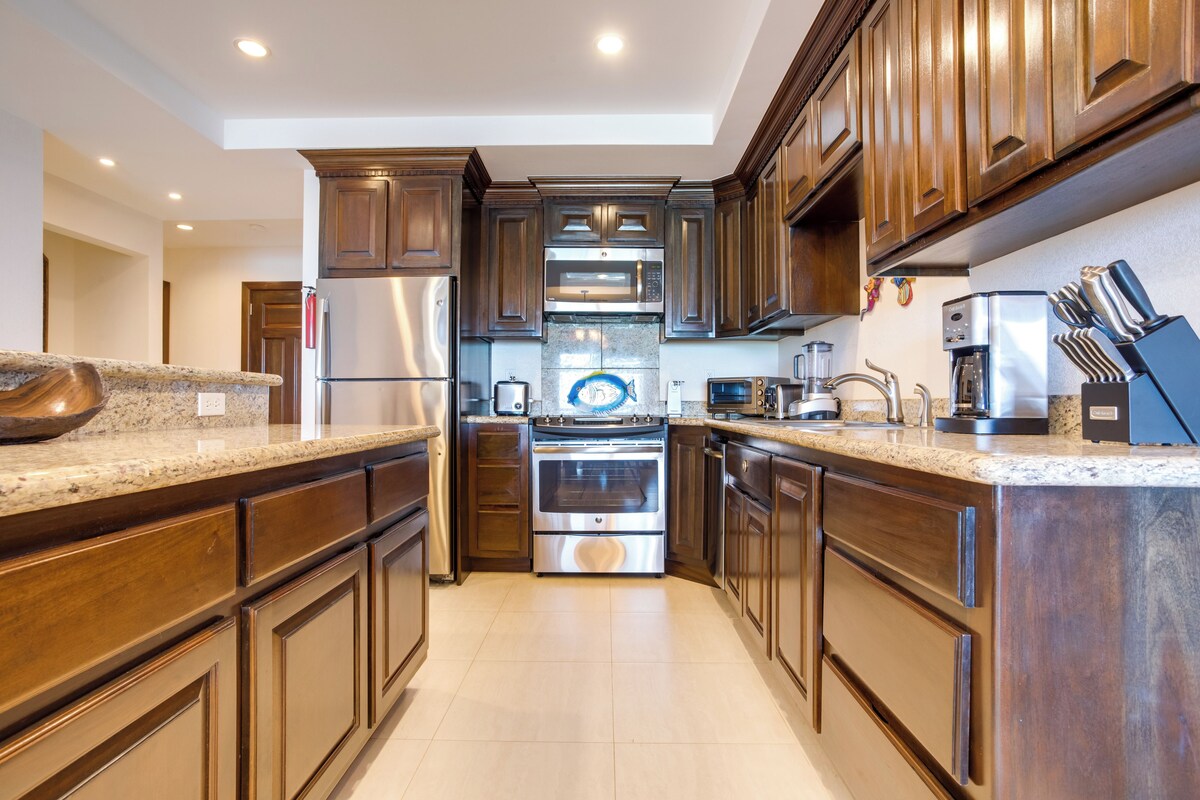 Una cocina moderna con armarios de madera, electrodomésticos de acero inoxidable, encimeras de granito y horno integrado.