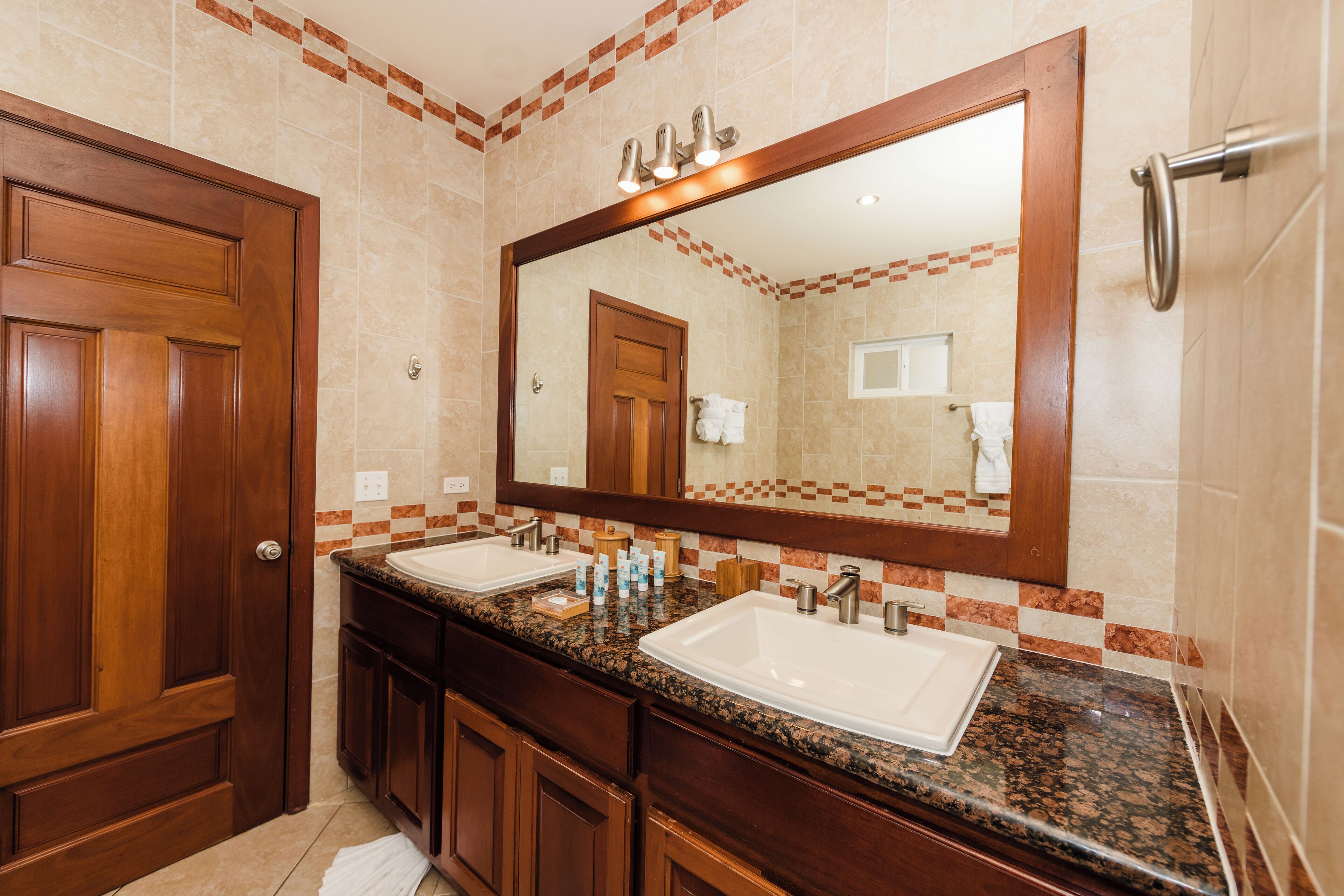 A bathroom with two sinks, a large mirror, wooden cabinets, and a tiled backsplash.