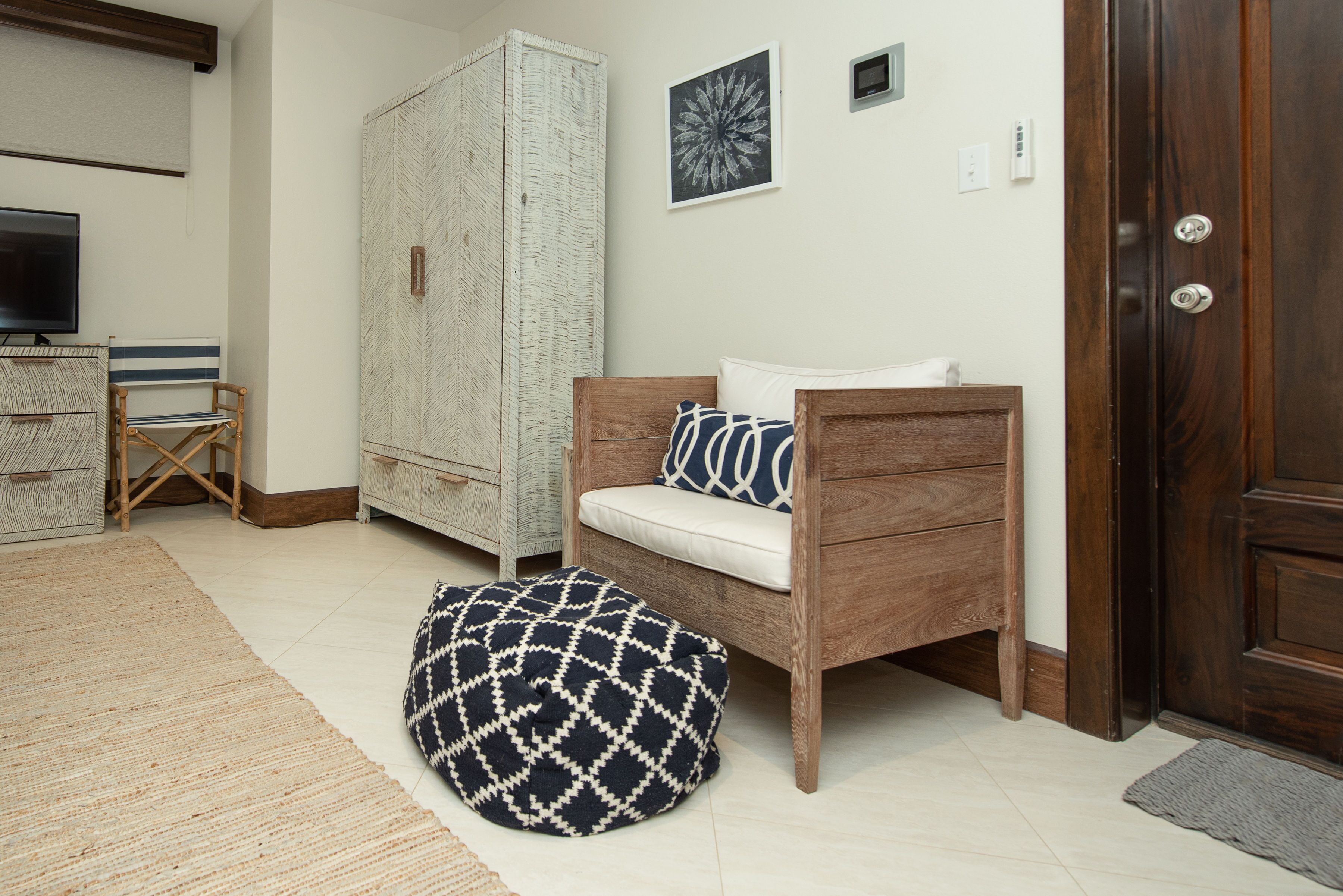 Una habitación con sofá de madera, un reposapiés estampado, televisor, armario y una obra de arte enmarcada en la pared.