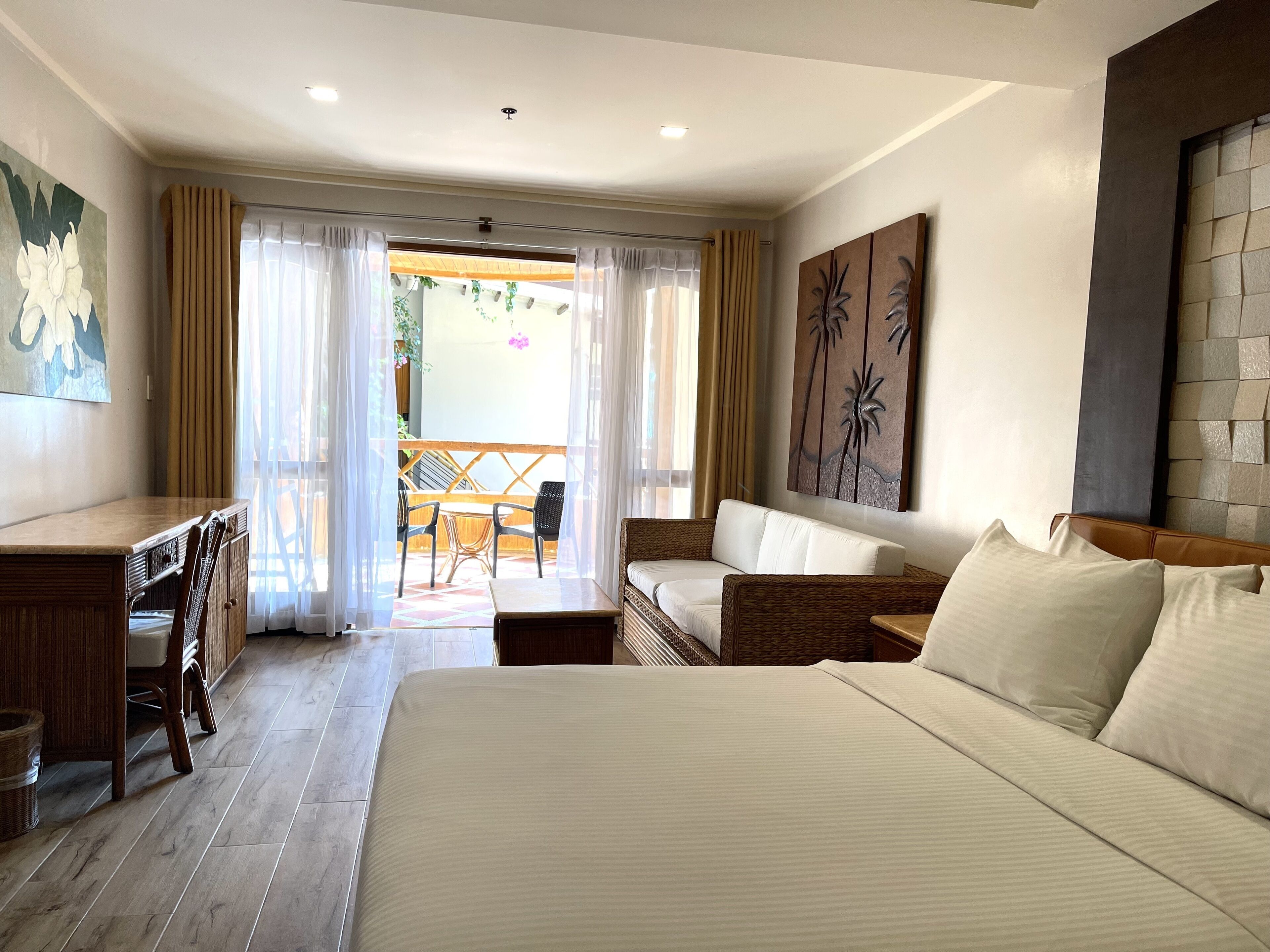Habitación de hotel con cama, escritorio, silla, sofá y balcón con mesa y sillas.