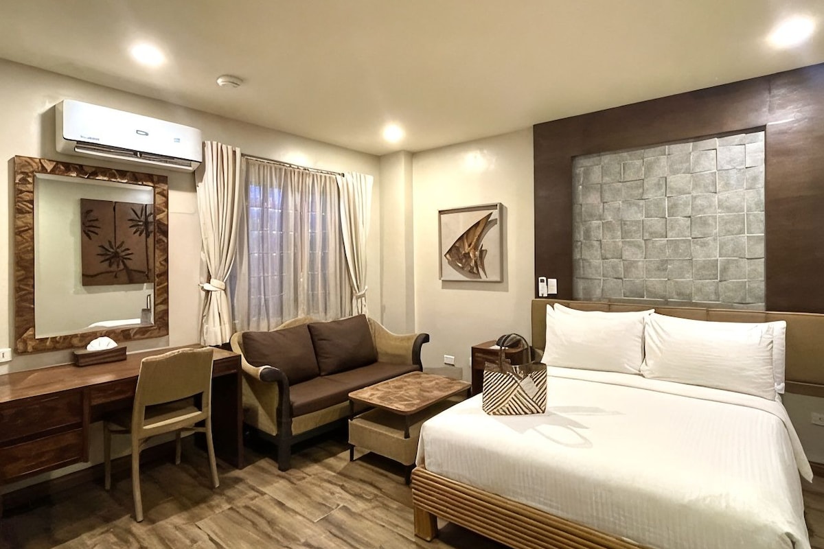 Habitación de hotel con cama, escritorio, sofá, sillón, mesita y aire acondicionado instalado en la pared.