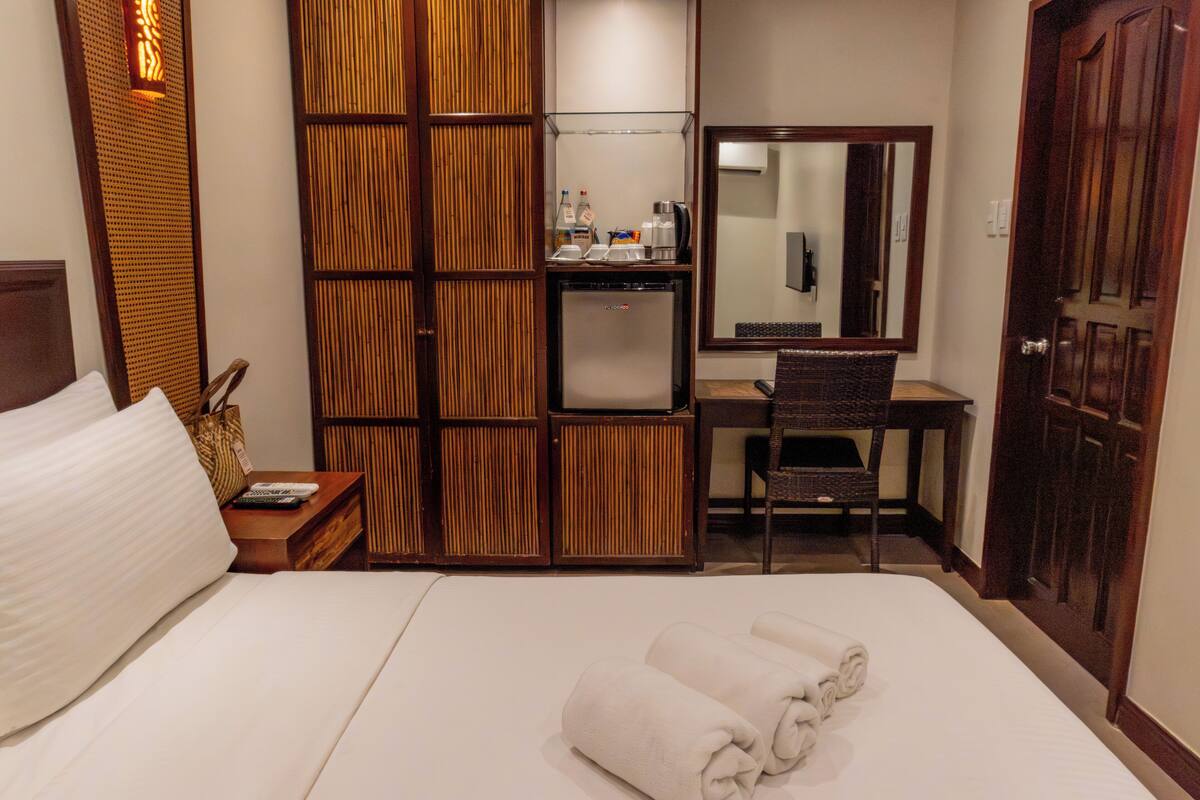 A hotel room with a bed, a desk with a chair, a wardrobe, and a minibar.
