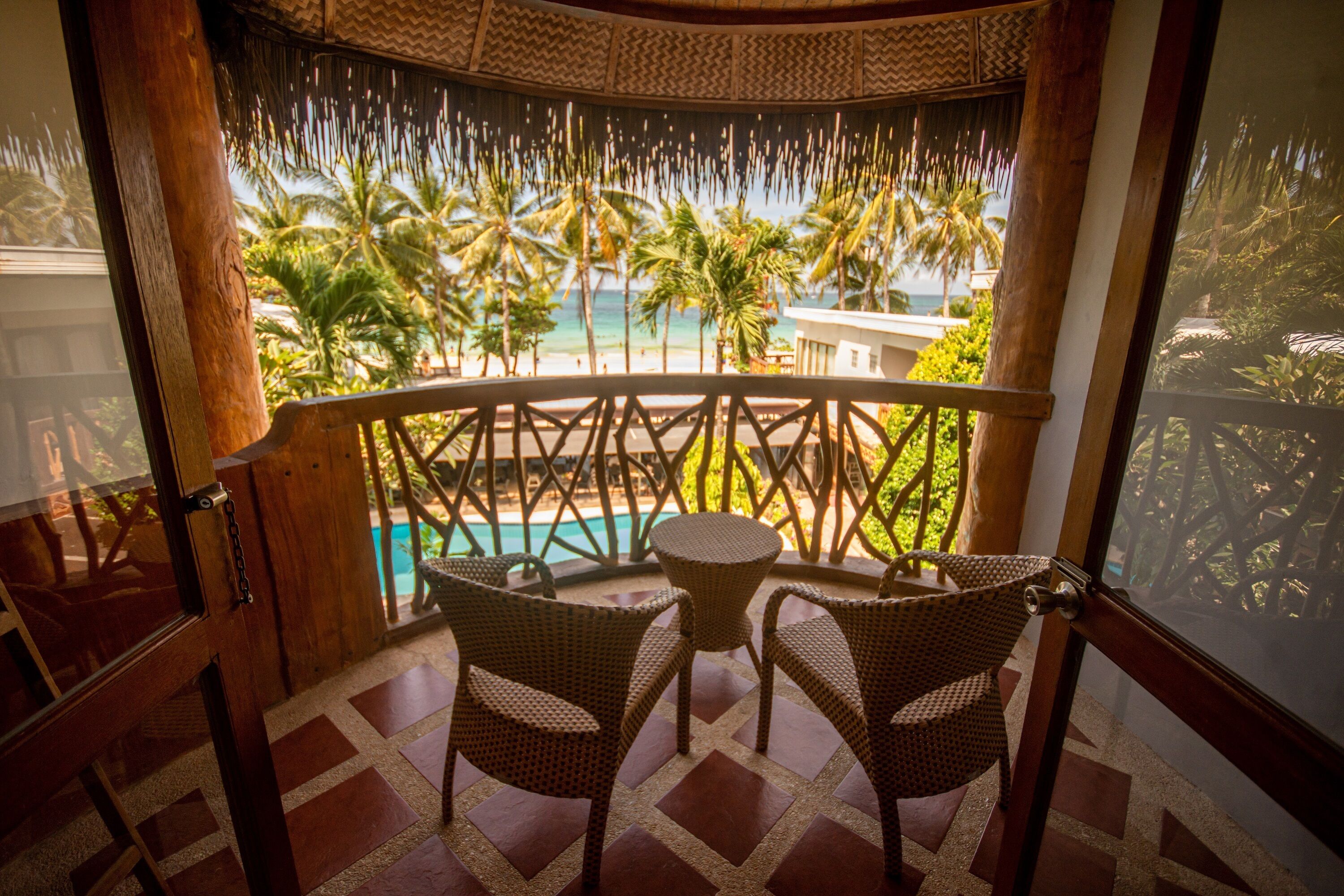 A balcony with wicker chairs and a table, overlooking a pool and palm trees.