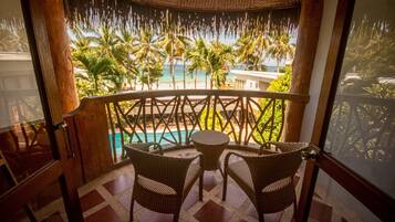 A balcony with wicker chairs and a table, overlooking a pool and palm trees.