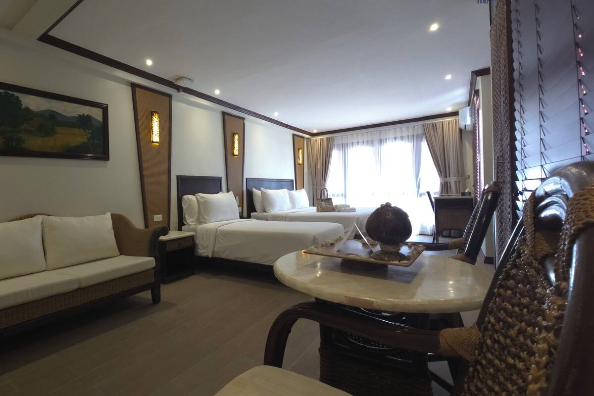 A hotel room with a sofa, two beds, a dining table, and a decorative sculpture.