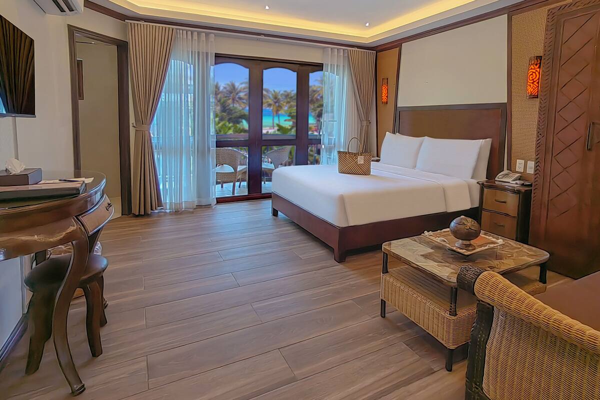 A hotel room with a bed, desk, chair, and a view of the outdoors.