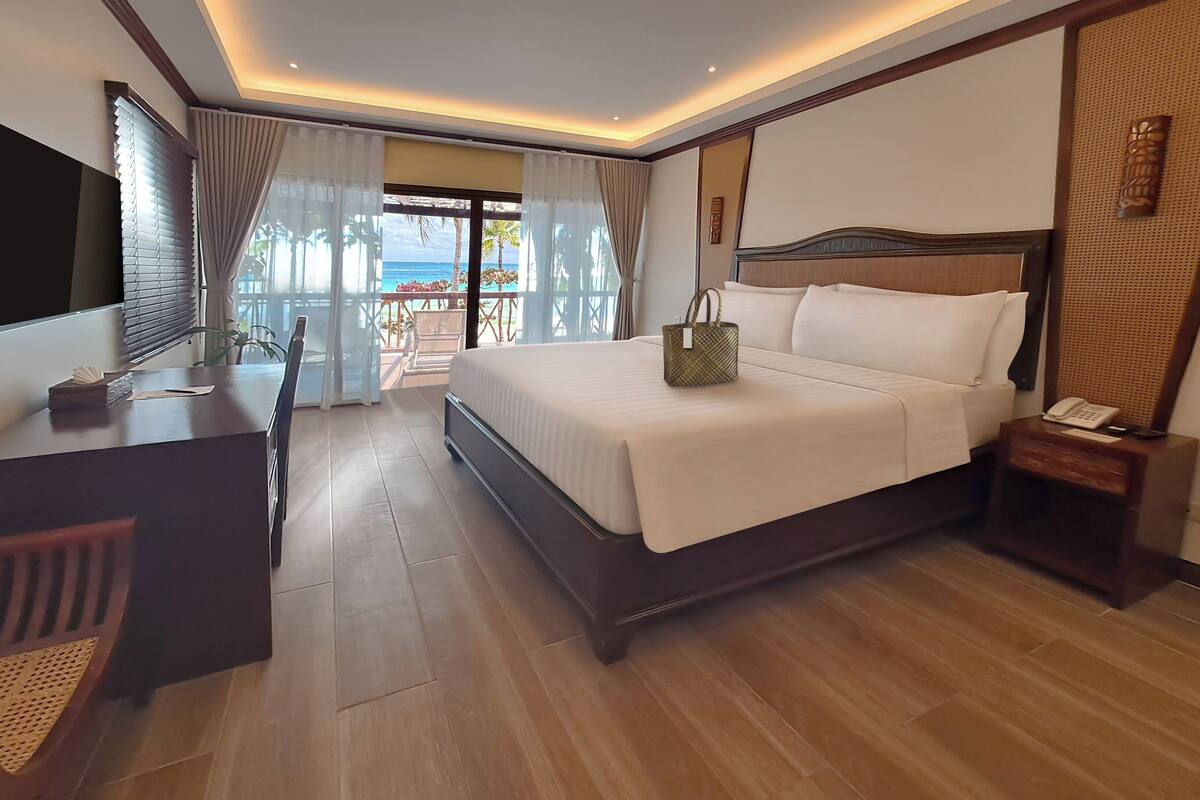 A hotel room with a large bed, a desk, a chair, a nightstand, and a TV.