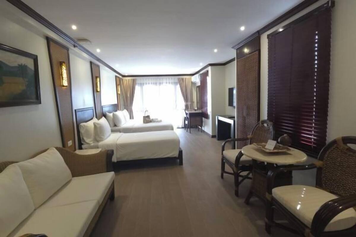 A hotel room with a bed, a sofa, a dining table with chairs, a TV, and a window with curtains.