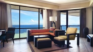 A modern hotel room with a large window offering a sea view, a sofa, a chair, a small table, and a lamp. - The Bellevue Resort (Panglao)