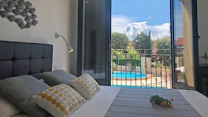 A bedroom with a bed, a nightstand, a lamp, and a view of a swimming pool outside.