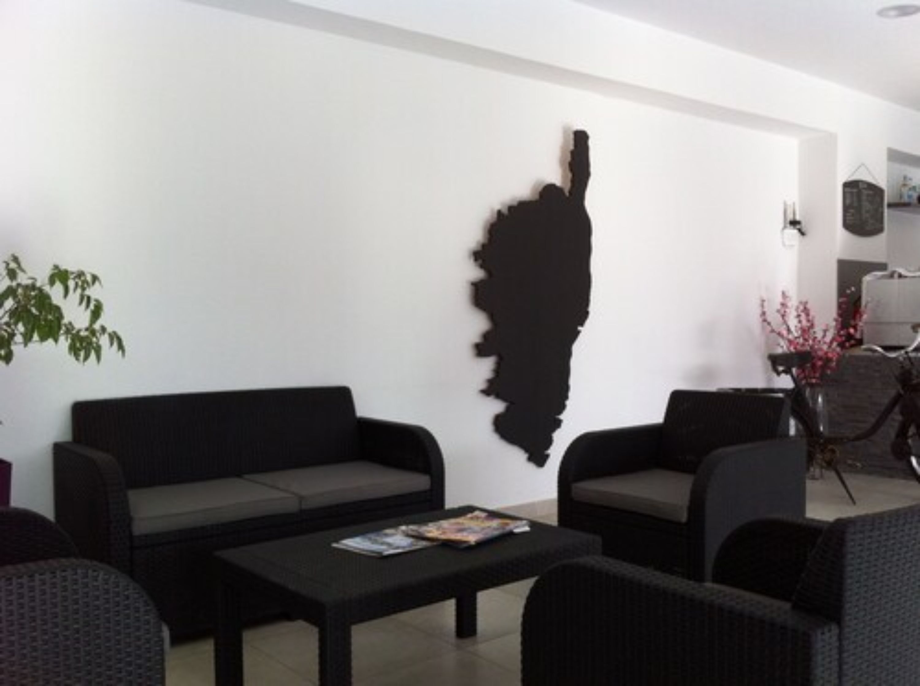 Un salon moderne avec une œuvre d’art abstraite noire au mur, un canapé gris, une table basse noire et un fauteuil en osier.