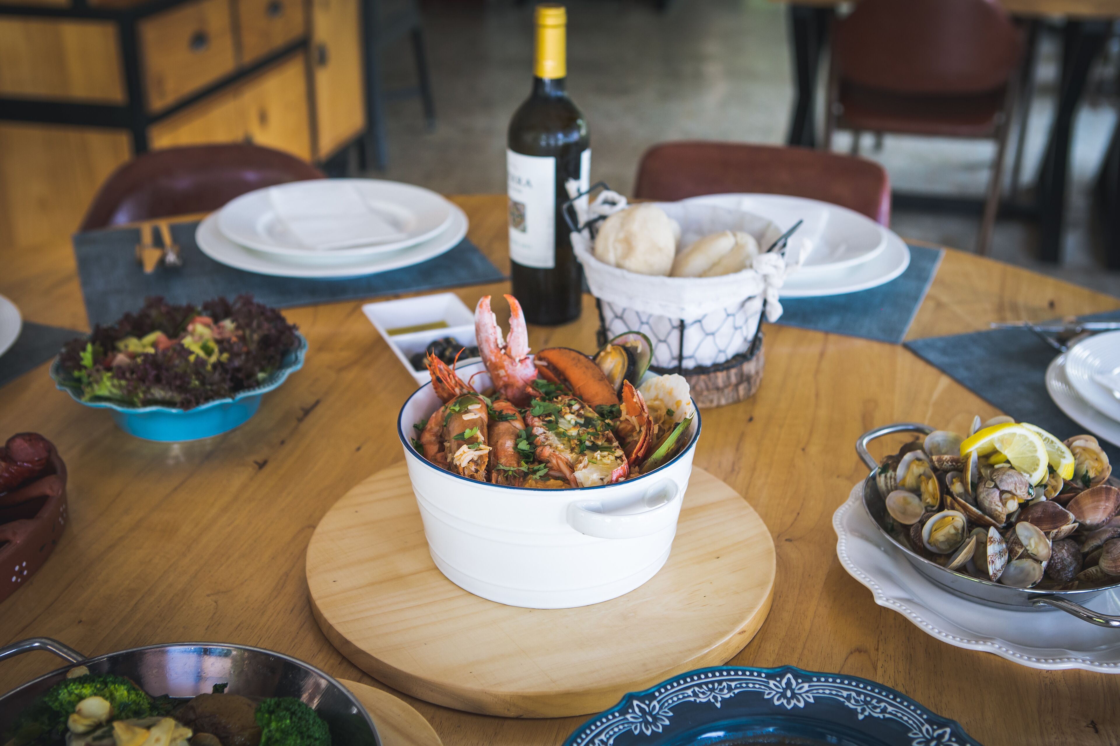 A dining table with various dishes, including seafood and bread, and a bottle of wine.
