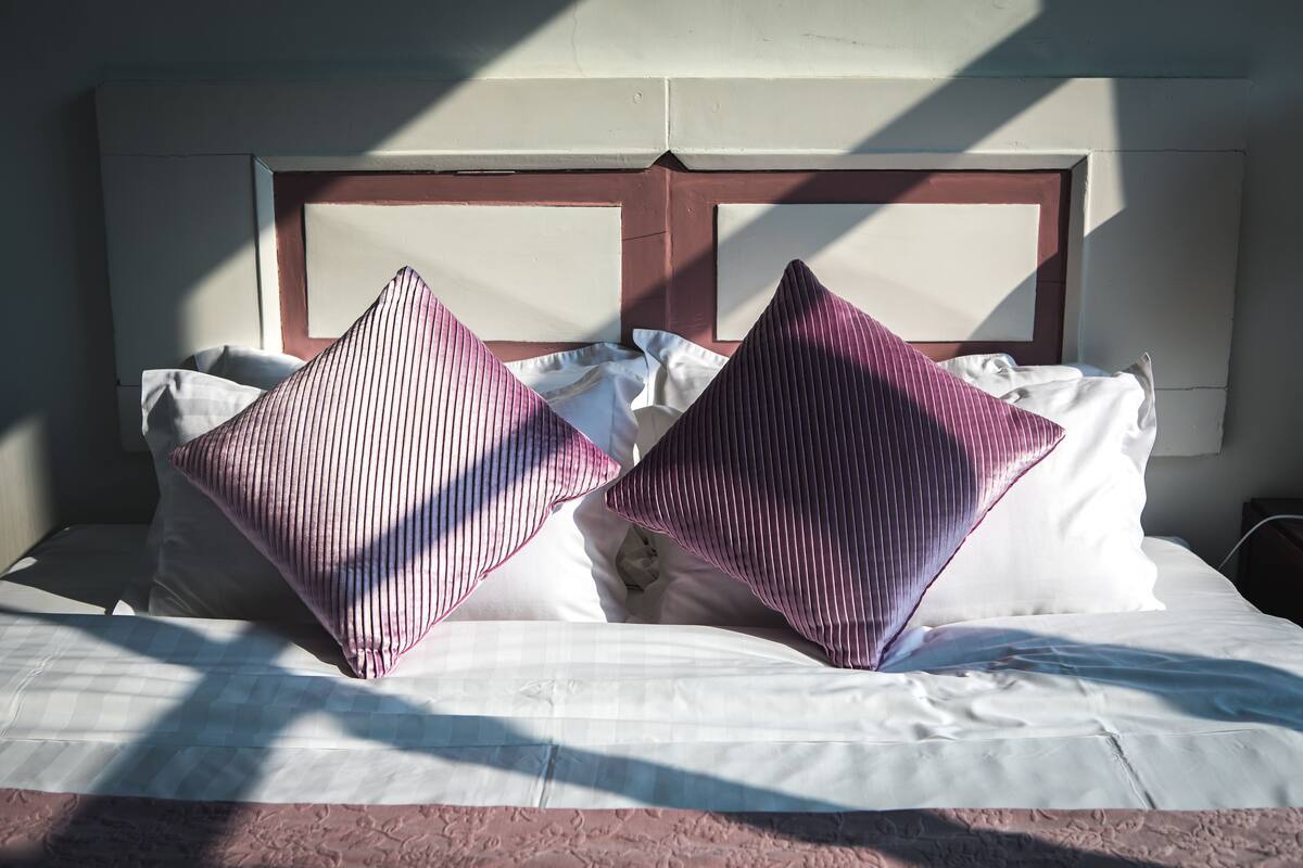 A bed with white linens and two large, striped pillows.