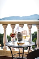Una mesa con una jarrón, dos vasos y un cuenco de fresas en un balcón con vistas a las montañas.