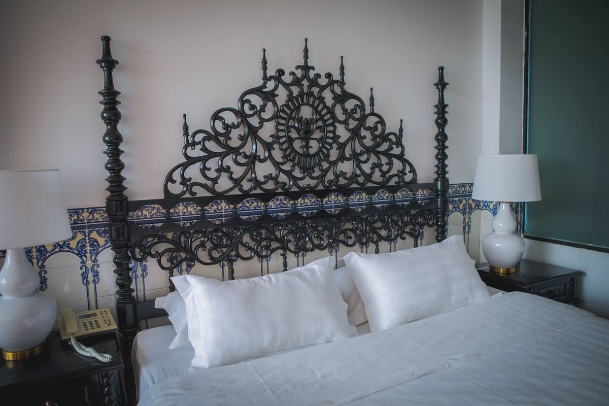 A neatly made bed with white linens, a decorative wrought iron headboard, and bedside lamps on either side.