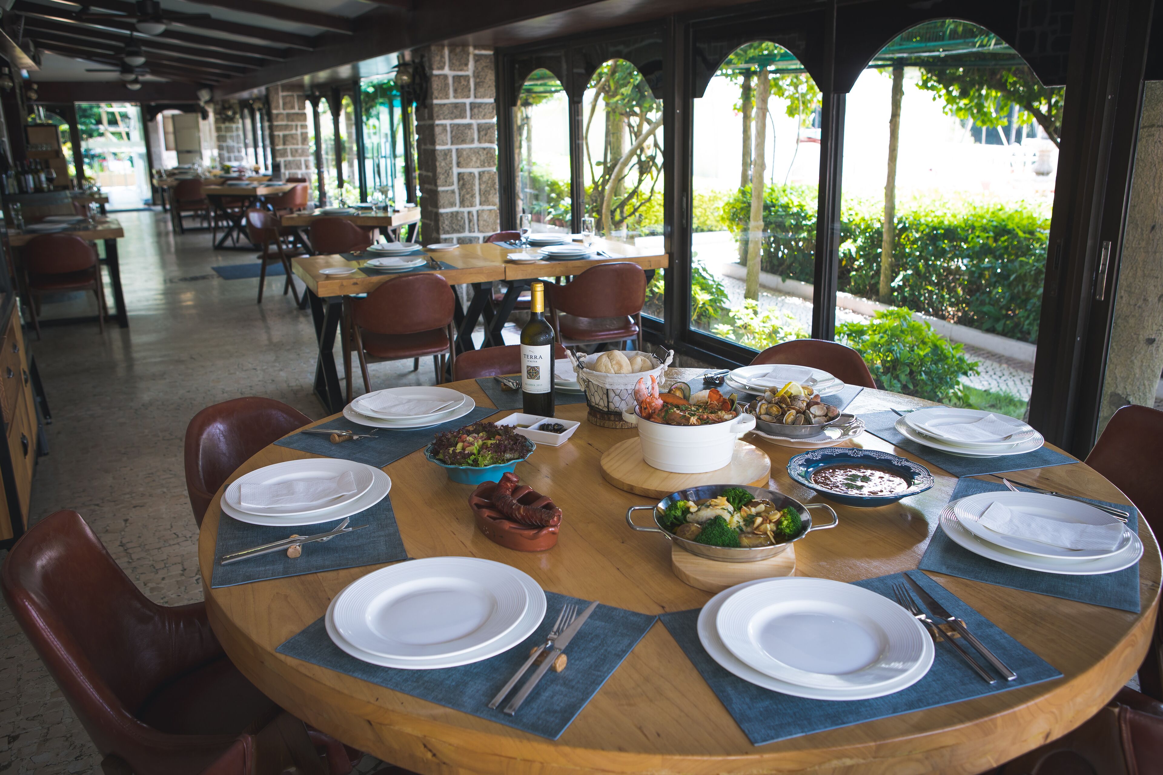 Un restaurant proposant des tables rondes, aménagé pour le service, avec un menu varié et une vue sur la verdure environnante.