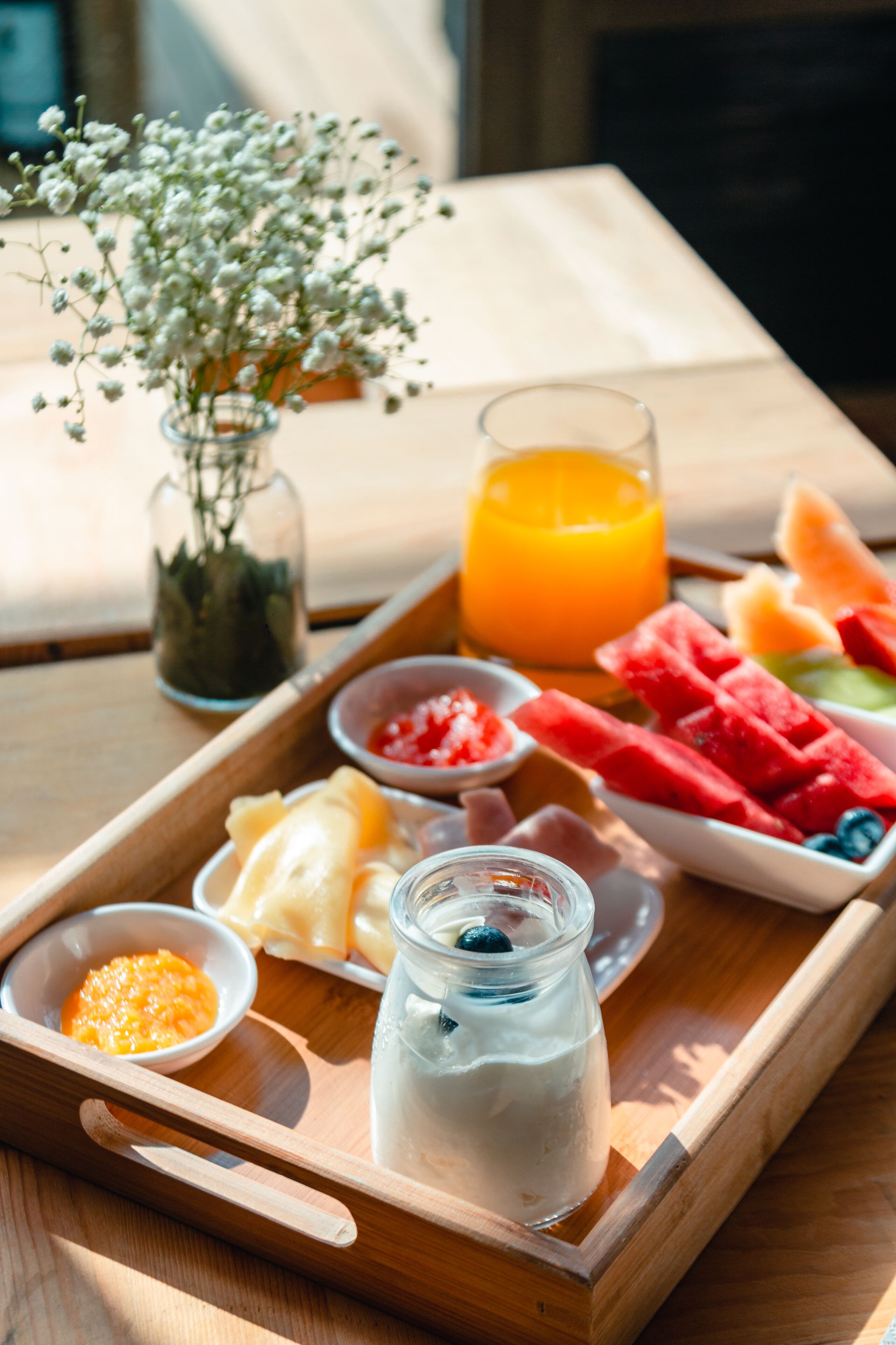 A wooden tray with a variety of breakfast items including yogurt, fruit, and juice.