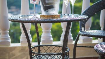 A table with a bottle of Soalheiro, two glasses of white wine, and a martini glass with strawberries on a balcony with a view of greenery.