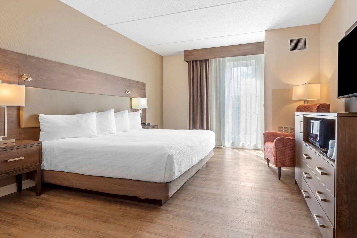Habitación de hotel con una cama grande, lámparas de noche, televisor, cómoda y ventana con cortinas.
