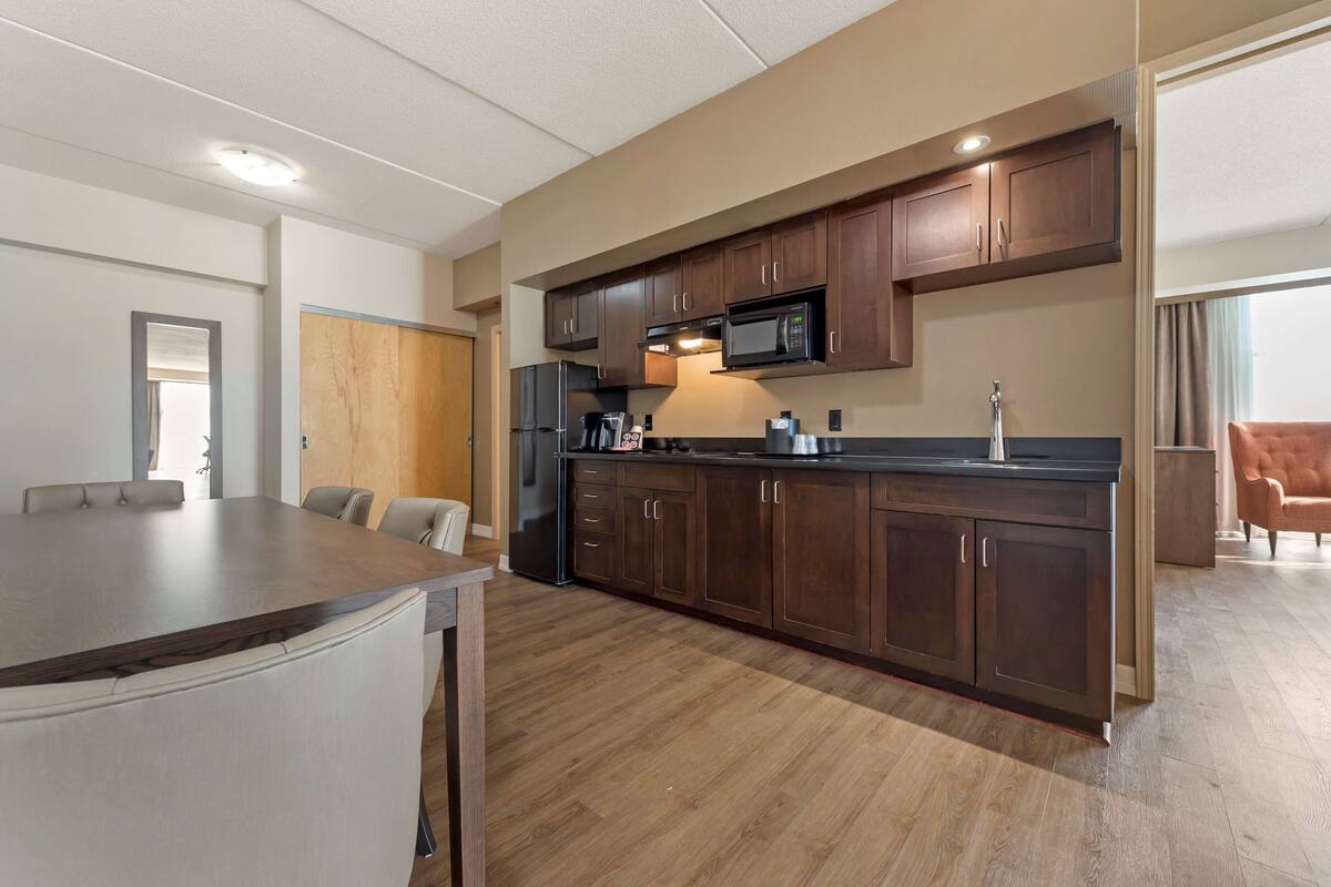 Una cocina moderna con armarios de madera oscura, un refrigerador de acero inoxidable y un microondas. Hay un comedor con una mesa grande y sillas.