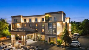 Un hotel de varios pisos con un patio central, entrada cubierta y zona de estacionamiento.