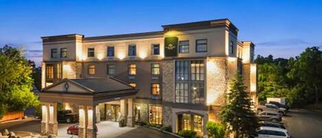 A multi-story hotel with a central courtyard, a covered entrance, and a parking area.