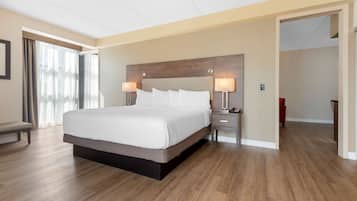 A modern hotel room with a large bed, bedside lamps, a bench, and a view through a window with curtains.