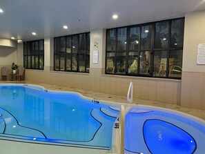 An indoor swimming pool with clear water, surrounded by beige walls and large windows.