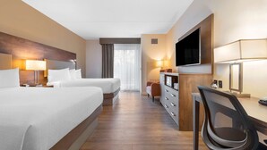 Una habitación de hotel con dos camas, un escritorio con silla, un televisor y un aparador.