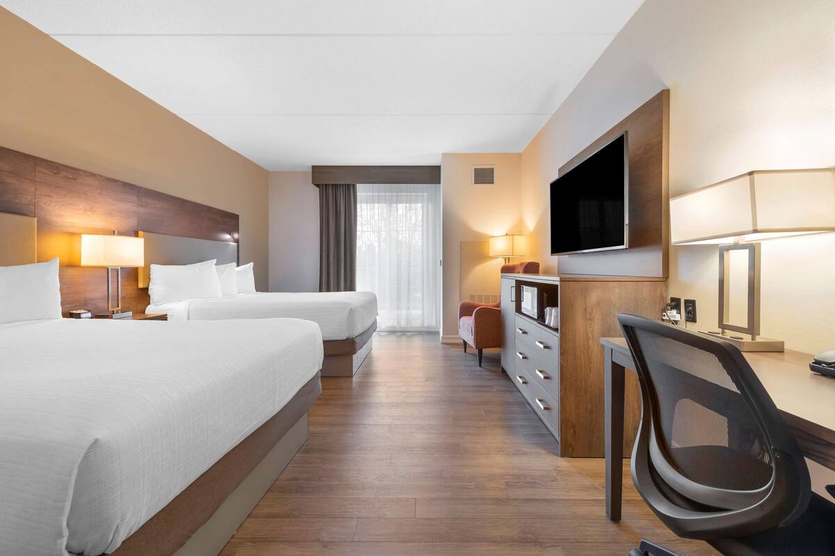 Una habitación de hotel con dos camas, un escritorio con silla, un televisor y un aparador.