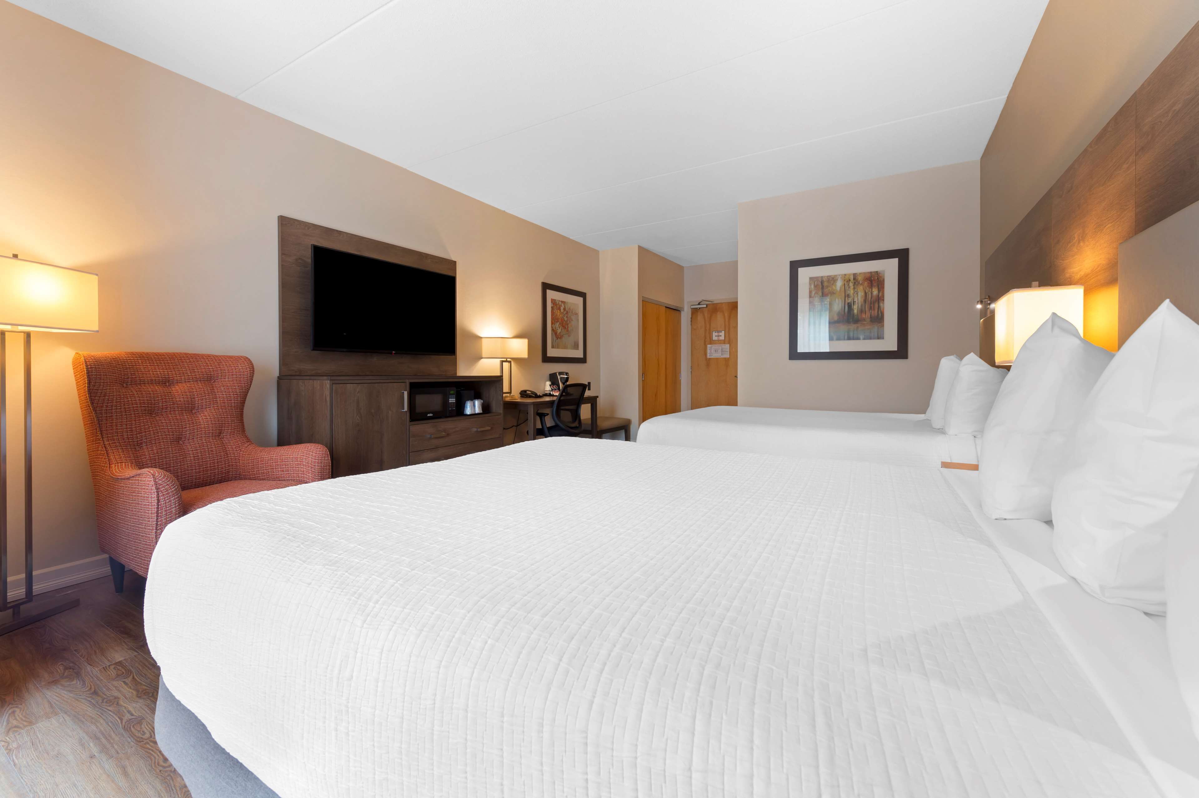 A hotel room with a large bed, a TV mounted on the wall, a desk with a chair, and two lamps.
