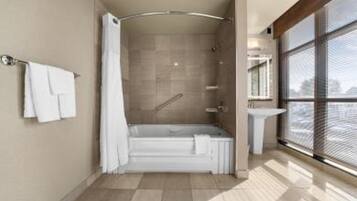 Ett modernt badrum med badkar, dusch och ett stort fönster som släpper in naturligt ljus.