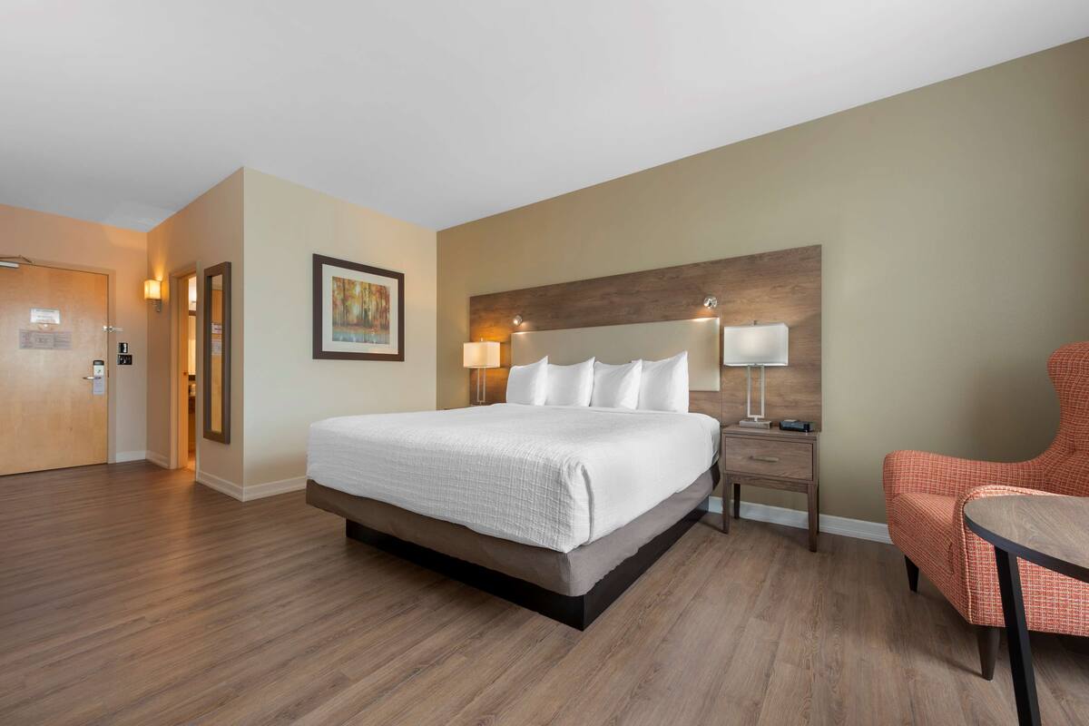 Habitación de hotel con una cama grande, una mesita de noche con lámpara, una silla y un cabecero de madera.