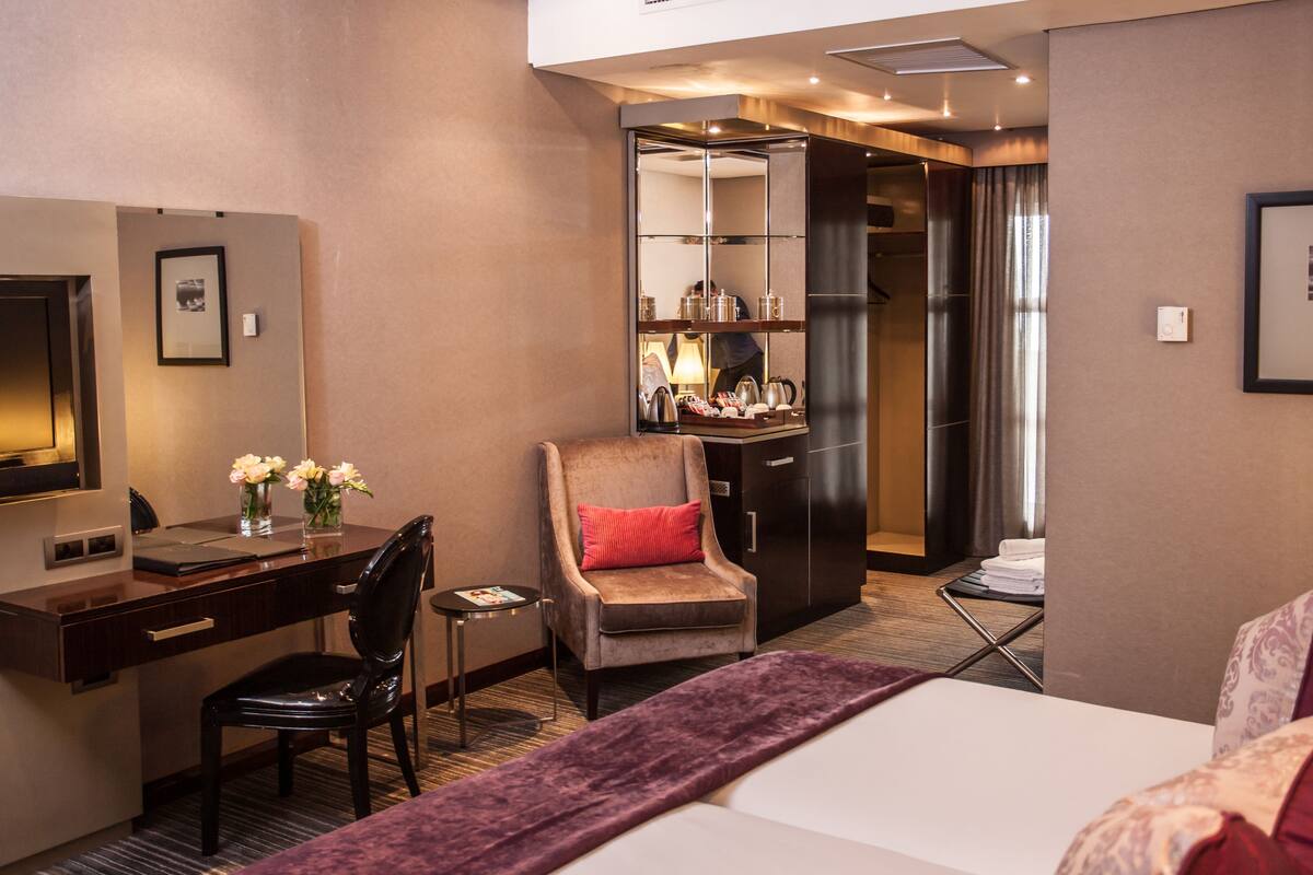 A hotel room with a bed, a desk, a chair, a small table, a mirror, a wardrobe, and a bathroom with a shower and toilet.