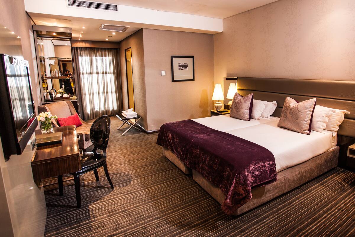 A hotel room with a large bed, bedside lamps, a desk with a chair, and a mirror.