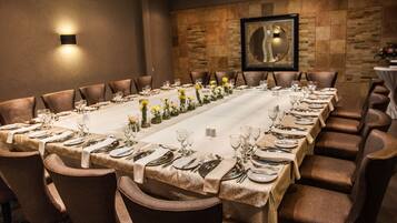 A long dining table set for a formal meal with multiple chairs, a framed artwork on the wall, and a textured wall behind the table.