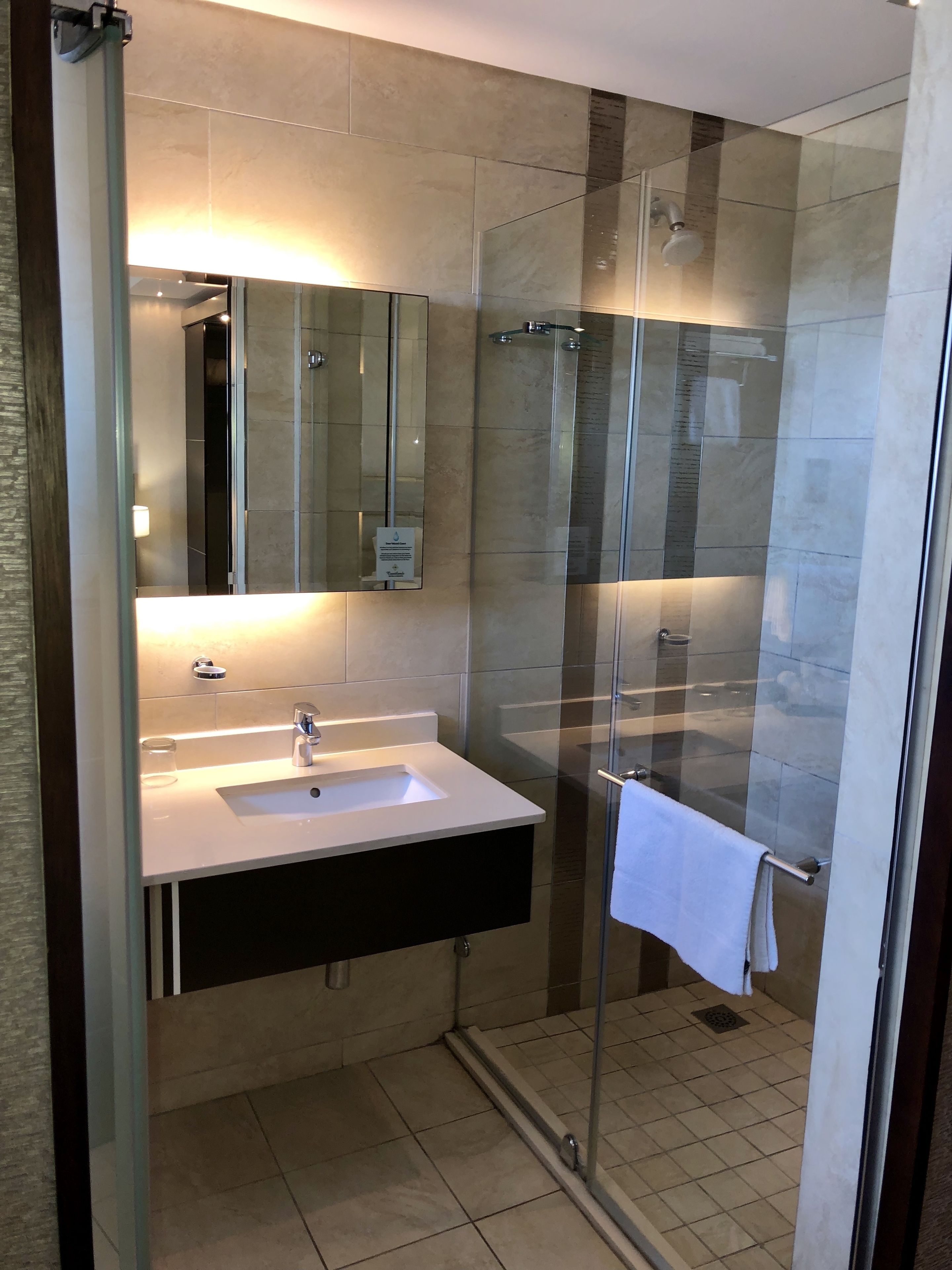 A modern bathroom with a glass shower enclosure, a sink with a mirror, and a towel hanging on a rack.