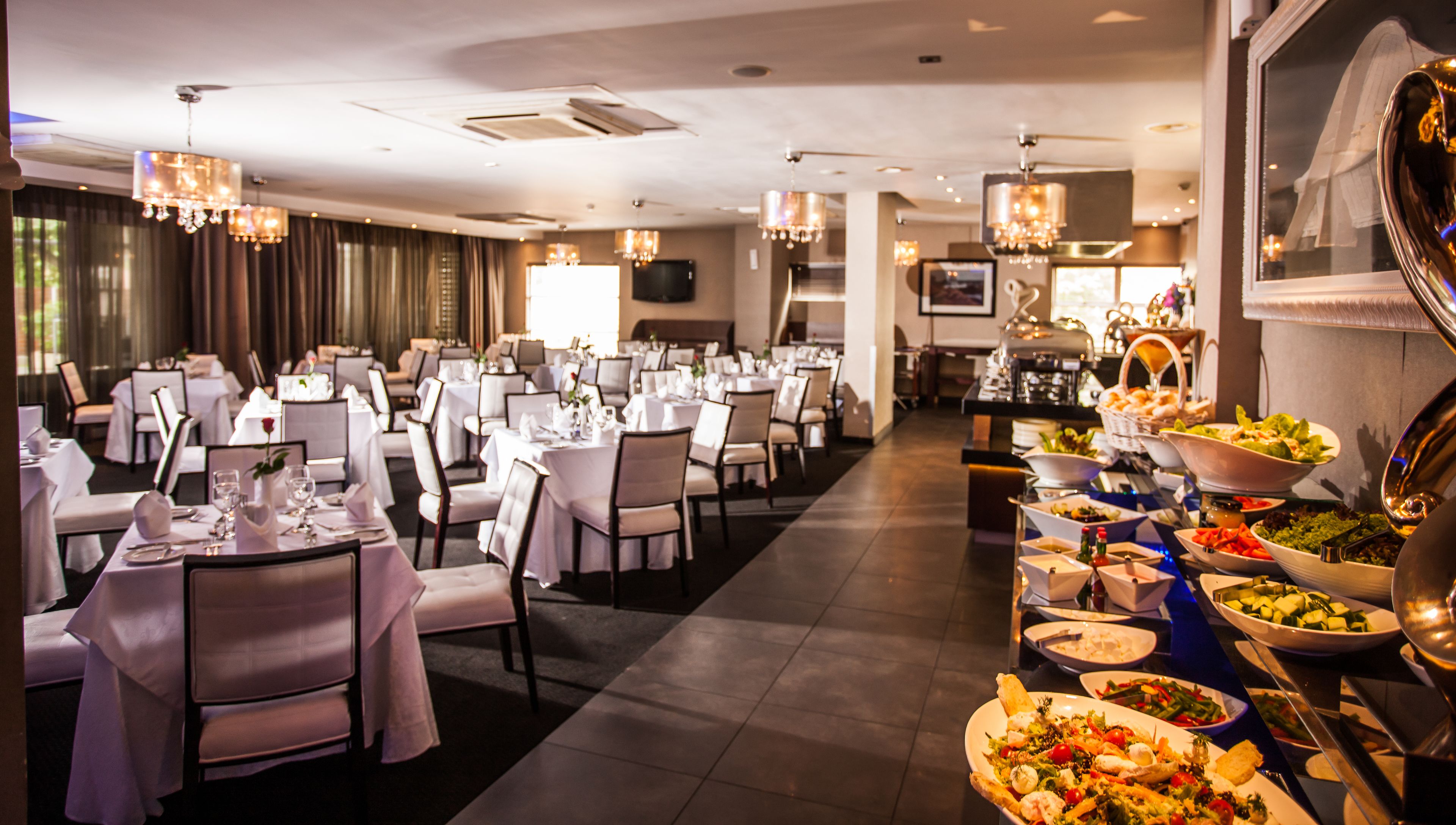 Un comedor de hotel con varias mesas dispuestas para los huéspedes, un bufé con diversos platos y elegantes candelabros.