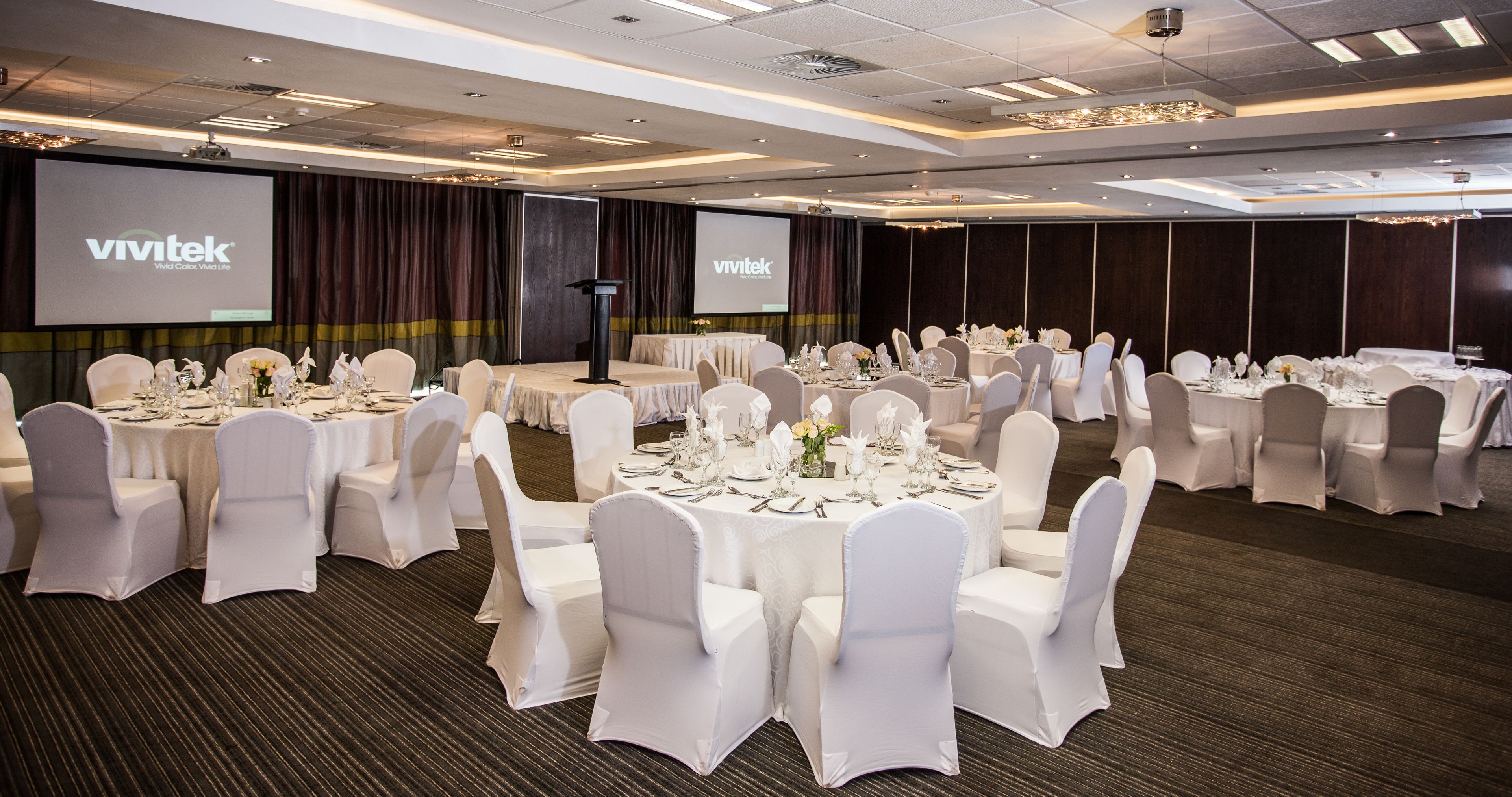 A banquet hall with round tables set for a formal event, featuring white chairs and table settings.