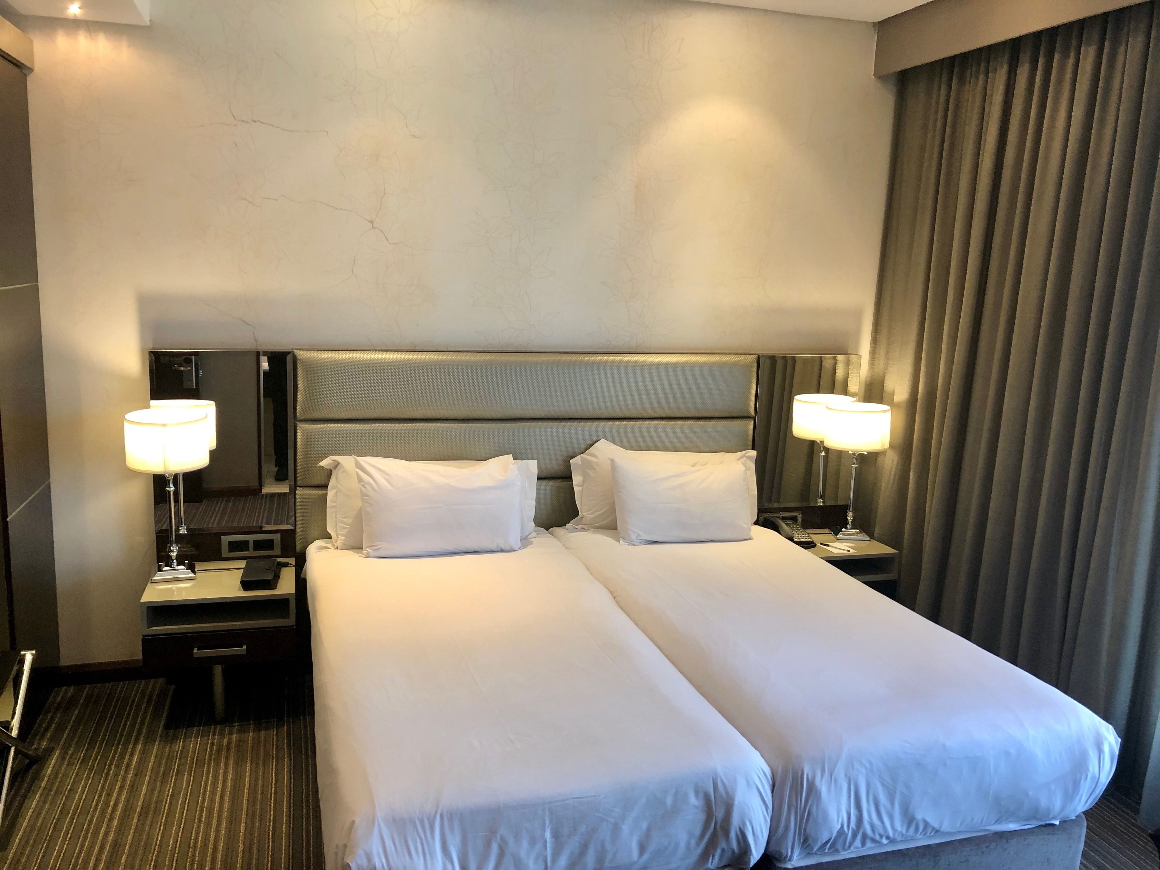Una habitación de hotel con una cama grande, dos mesitas de noche, un espejo y una cortina.