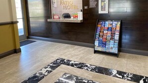 A reception area with a reception desk, a bulletin board with brochures, and a dark wooden wall. - Patio Motel (Gardena)