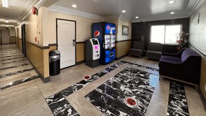 A hotel lobby with a marble floor, a Pepsi vending machine, seating area, and a door. - Patio Motel (Gardena)