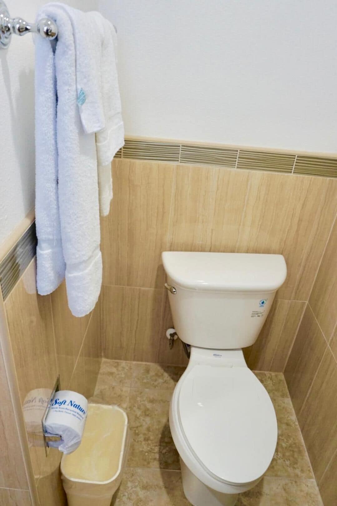 A bathroom with a toilet, a towel rack with towels, and a toilet paper holder.