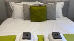A neatly made bed with white linens and two folded towels on a green mat.