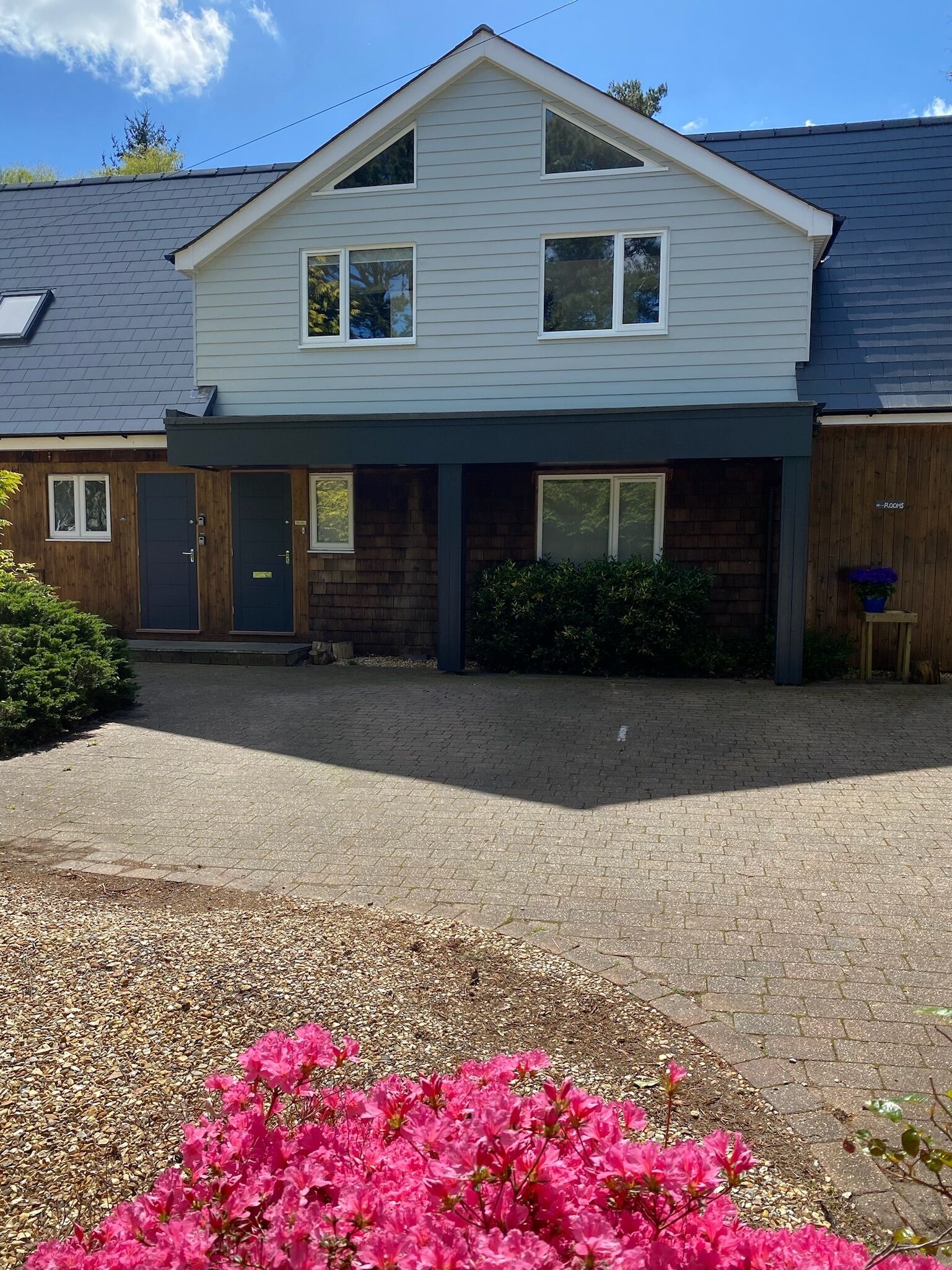 A two-story house with a front porch, a driveway, and a garden with pink flowers.