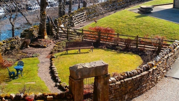 A landscaped garden with a stone wall, a wooden fence, and a bench. - Riverside B & B (Leyburn)