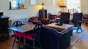 A spacious room with exposed wooden beams, a large table, several upholstered chairs, and a radiator. - Riverside B & B (Leyburn)