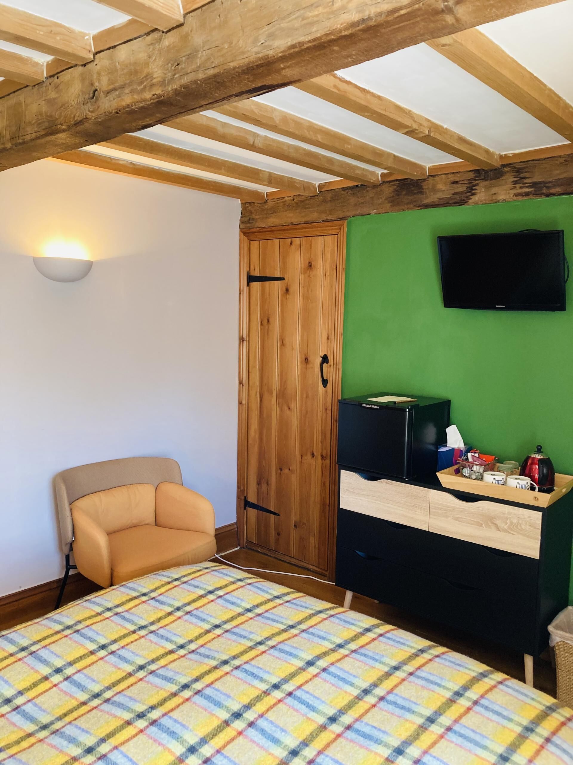 A bedroom with a bed, a chair, a wardrobe, a television, and a desk with various items.